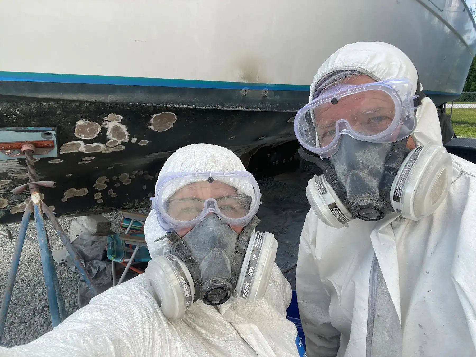 Matt and Linda in protective coveralls and respirators working under their boat during the renovation phase of Life Afloat: The Boat Season